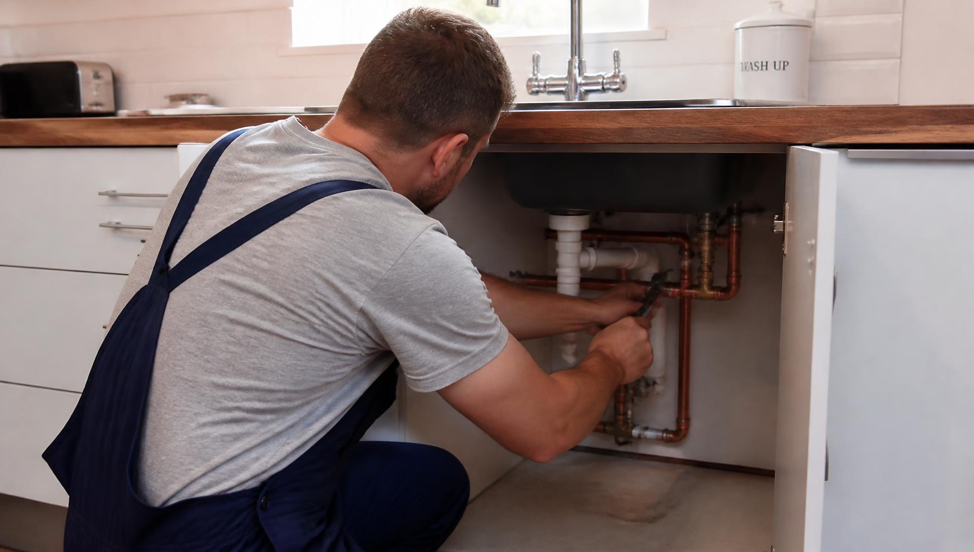 Local plumber working on pipework under a kitchen sink in a Swansea home